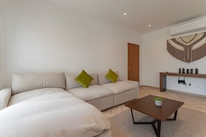 Un salon moderne avec un canapé d’angle, une table basse et une petite table d’appoint agrémentée d’une plante.