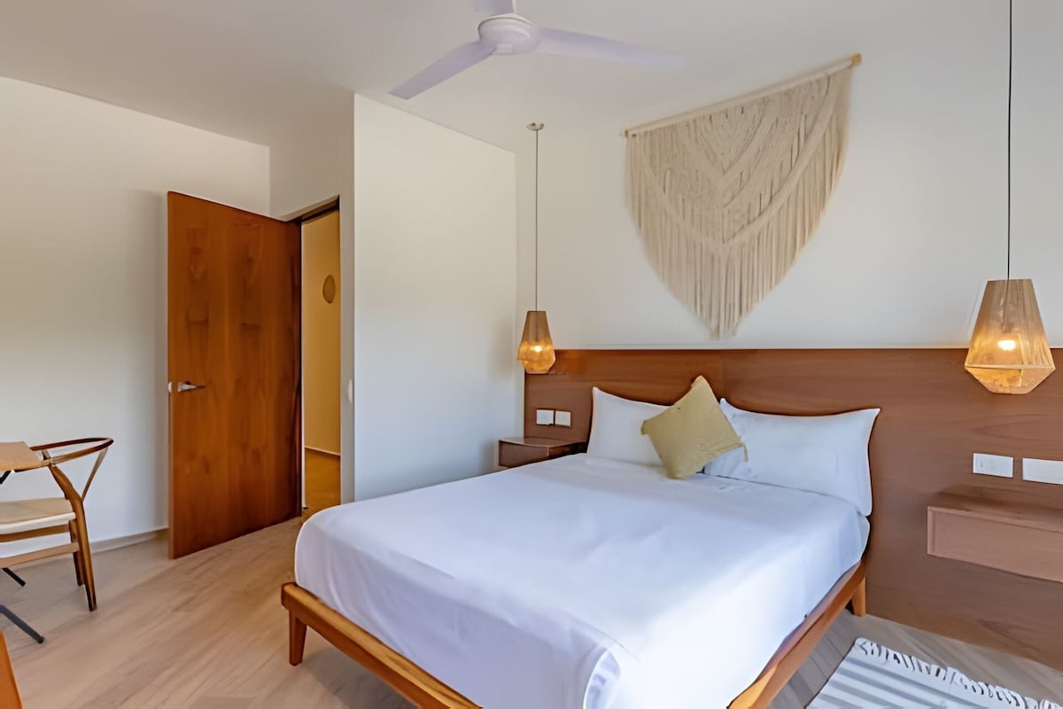 A neatly arranged bedroom with a bed, bedside tables, a ceiling fan, and a wall-mounted macrame piece.
