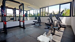 A gym with a squat rack, bench press, and various weight machines, with large windows offering a view of palm trees. - oasis yaaxlum (Tulum)