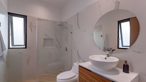 A modern bathroom with a marble wall, a large round mirror, a white sink, and a toilet. - oasis yaaxlum (Tulum)