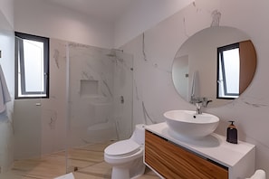 A modern bathroom with a marble wall, a large round mirror, a white sink, and a toilet. - oasis yaaxlum (Tulum)