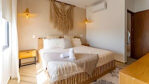 A spacious bedroom with a large bed, two bedside tables, a wooden nightstand, a hanging tapestry, and a wooden wardrobe. - oasis yaaxlum (Tulum)