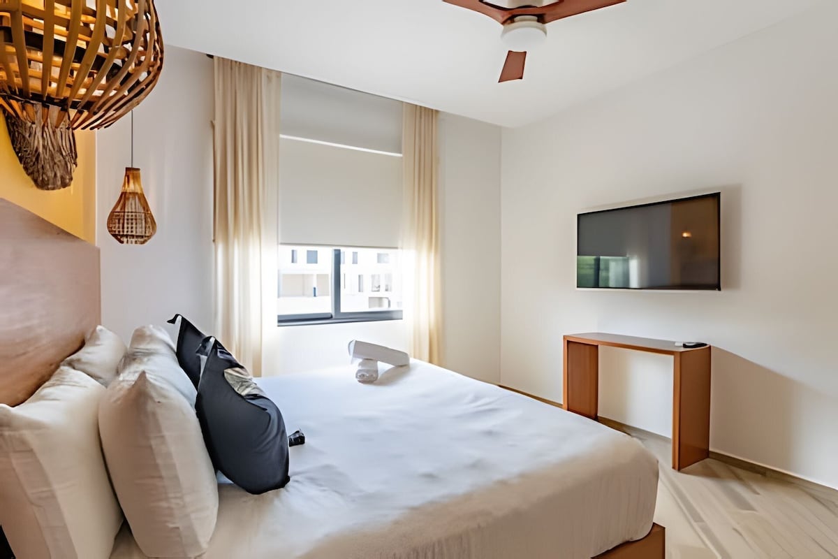 A modern hotel room with a large bed, a desk, and a TV on the wall.
