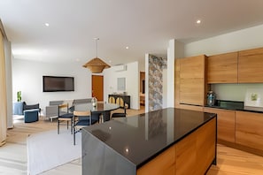 A modern kitchen with wooden cabinets, a black countertop, and a dining area with a round table and chairs. - oasis yaaxlum (Tulum)