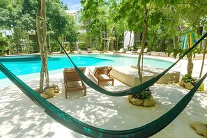 Zona de piscina con una hamaca, sillas de descanso y una pequeña isla con rocas.
