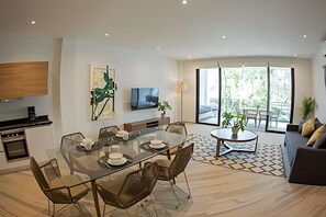 A modern living room with a glass dining table, comfortable seating, a flat-screen TV, and a large window offering a view of the outdoors. - oasis yaaxlum (Tulum)