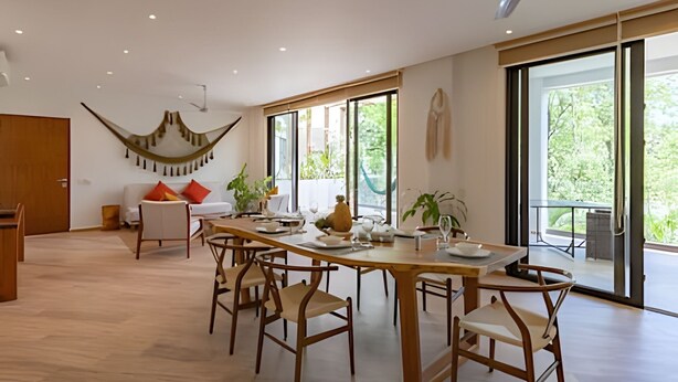 A spacious dining area with a long table and chairs, a ceiling fan, and large windows offering a view of greenery outside. - oasis yaaxlum (Tulum)