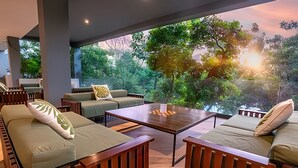 A modern outdoor seating area with cushioned sofas and a central coffee table, overlooking a lush garden. - oasis yaaxlum (Tulum)