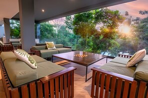 A modern outdoor seating area with cushioned sofas and a central coffee table, overlooking a lush garden. - oasis yaaxlum (Tulum)