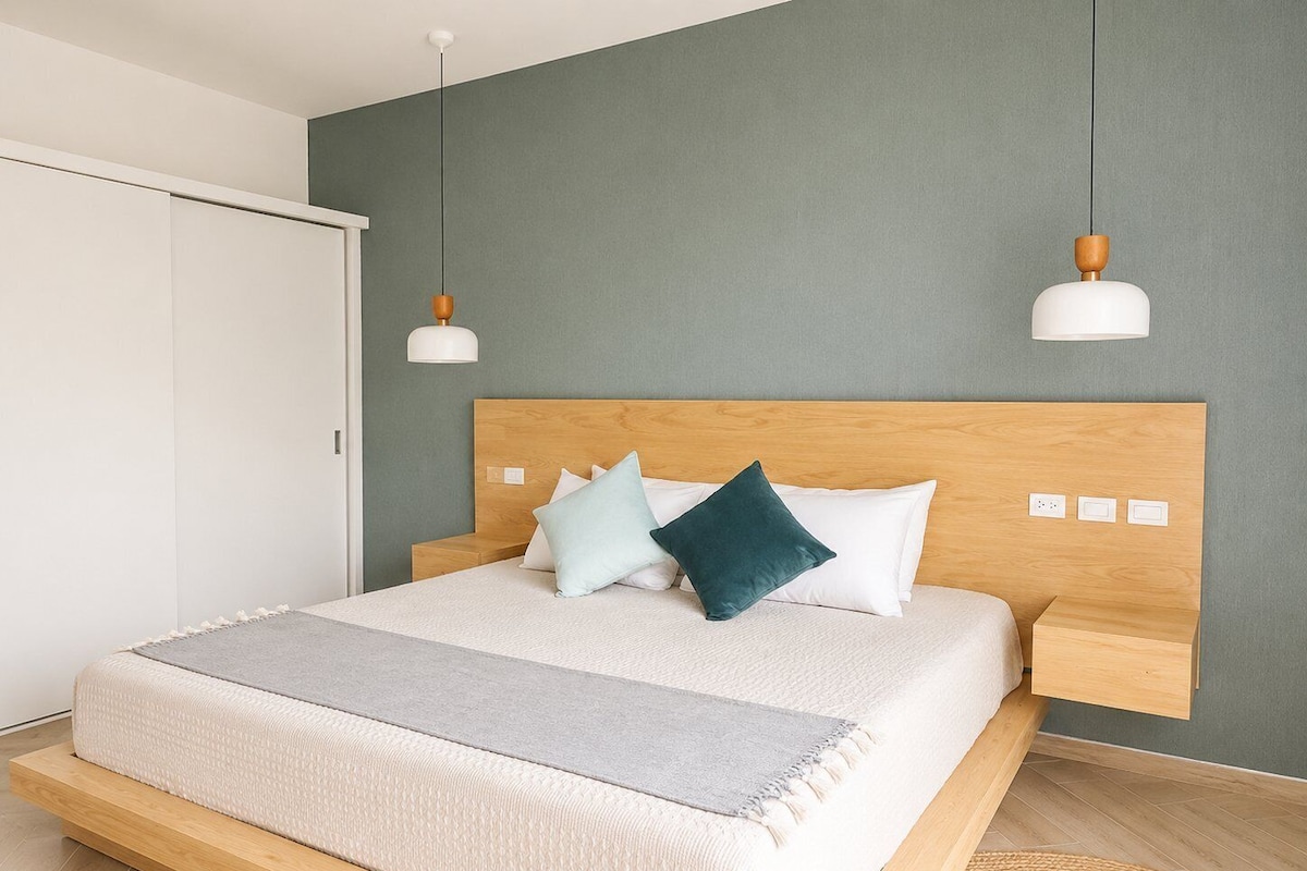 A modern bedroom with a wooden bed frame, a grey wall, and a white wardrobe.