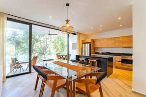 A modern kitchen with wooden cabinets, a glass dining table, and a large window overlooking a forest. - oasis yaaxlum (Tulum)