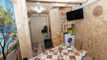 Ein gemütlicher Raum mit Holzboden, einem Tisch mit kariertem Tuch, einer Waschmaschine, einer Mikrowelle und einem an der Wand befestigten Fernseher.