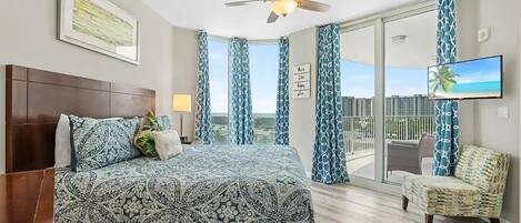 A hotel room with a large bed, a ceiling fan, a TV, a balcony with a view, and a chair.