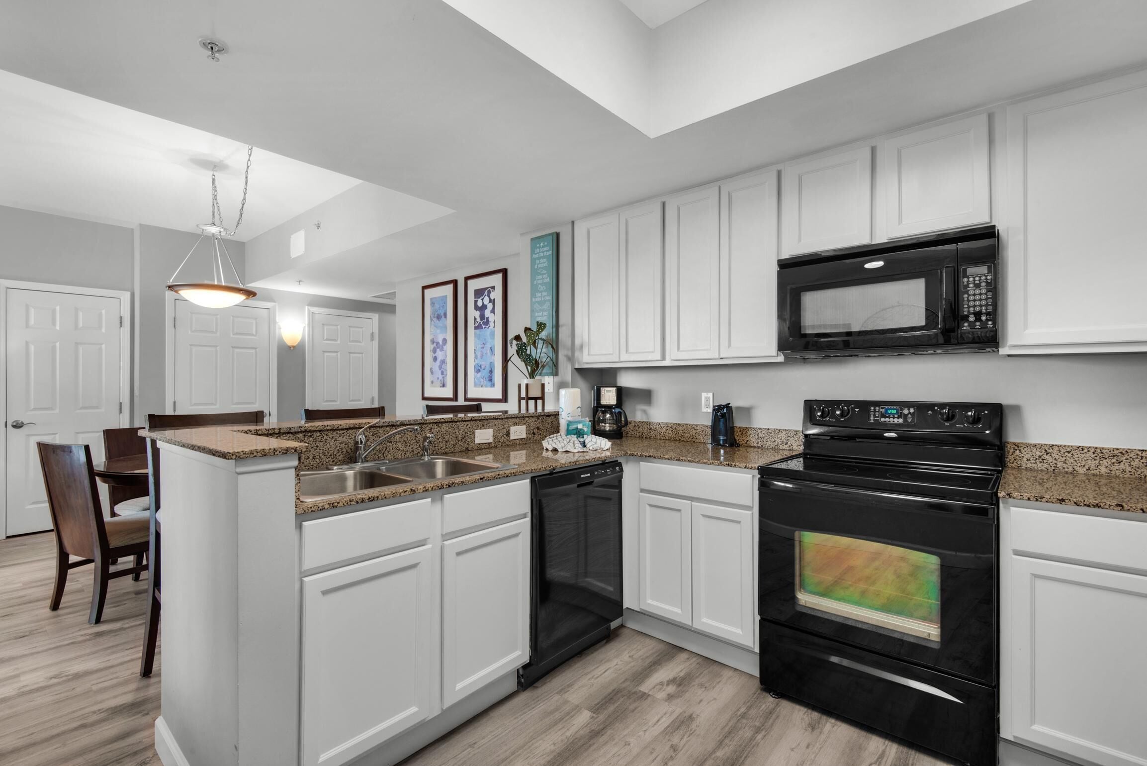 A modern kitchen with white cabinetry, a granite countertop, a built-in microwave, and a black oven.