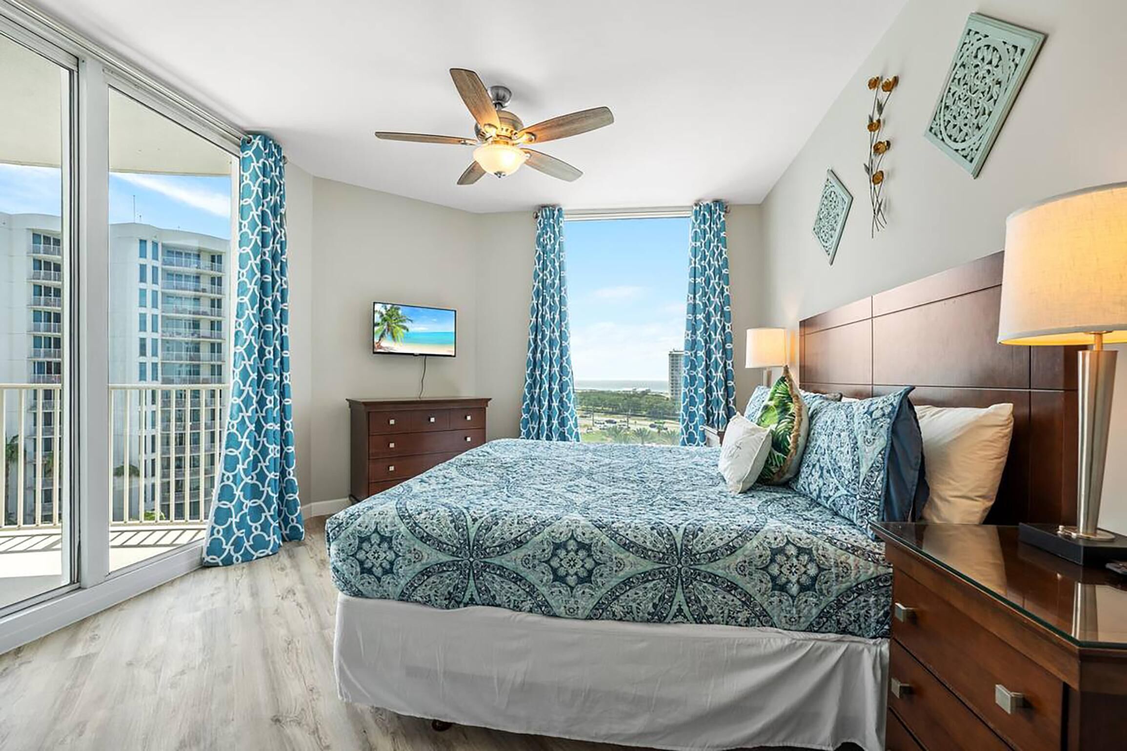 A bedroom with a bed, a ceiling fan, a TV, and a view of the city.
