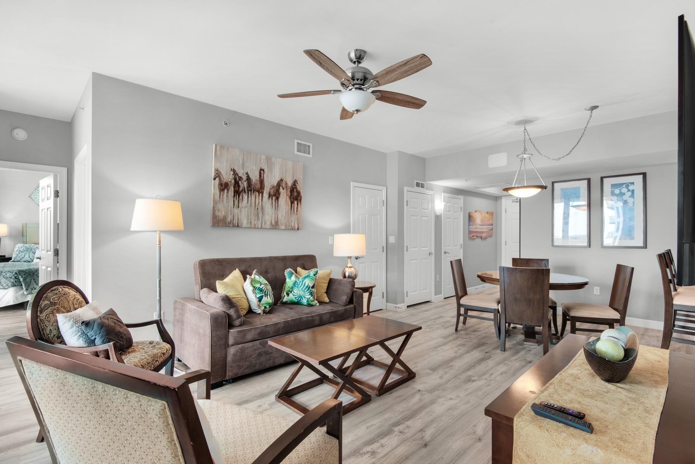 A modern living room with a sofa, coffee table, and chairs. There is a ceiling fan, a lamp, and artwork on the walls.