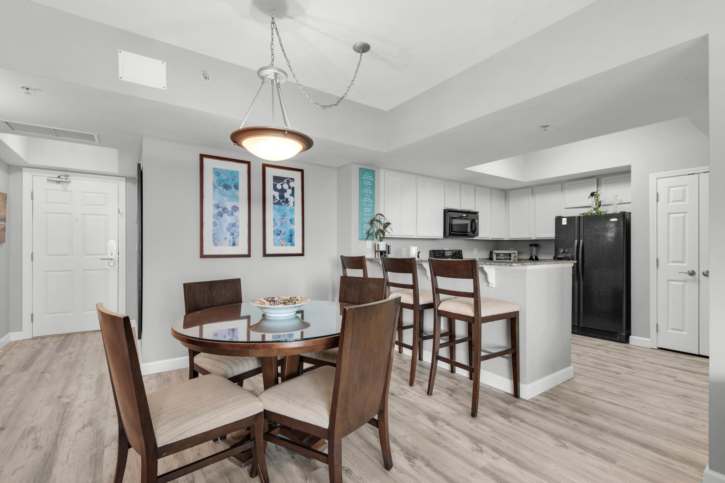 A modern kitchen with white cabinets, a black refrigerator, and a dining area with wooden chairs and a round table.