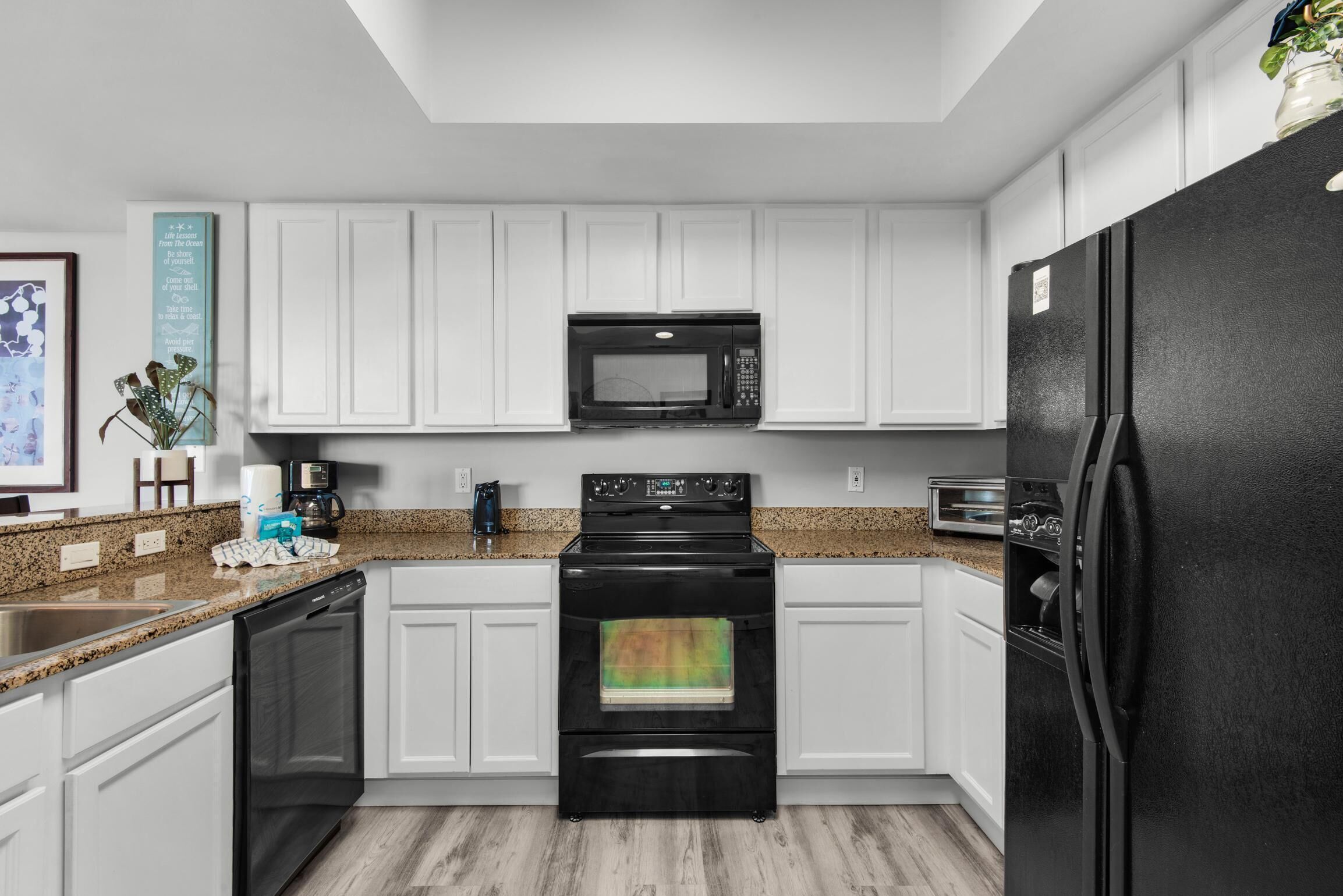 Una cocina moderna con armarios blancos, un refrigerador negro, un microondas, un horno y un lavavajillas.