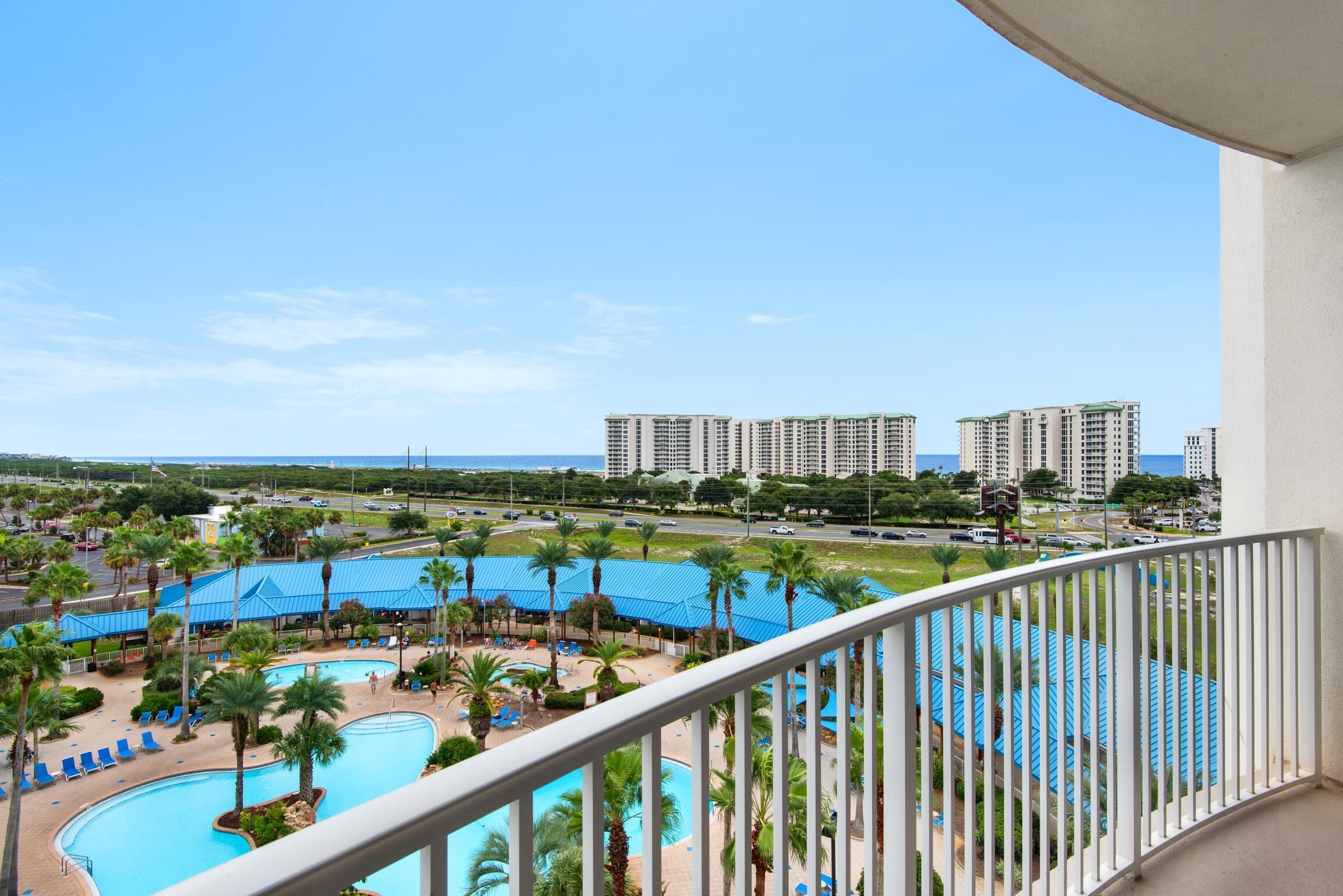 A view of a resort with a swimming pool, palm trees, and high-rise buildings in the background.