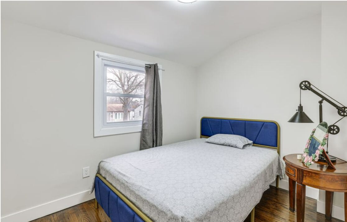 A single bed with a blue headboard in a room with white walls and a window with curtains.