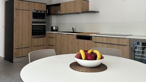A modern kitchen with wooden cabinets, a built-in oven, and a dining area with a round table and chairs.