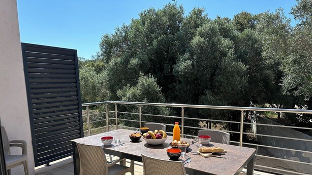 A balcony with a table set for breakfast, including fruits, bread, and a beverage.