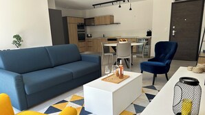 A modern living room with a blue sofa, a yellow armchair, and a white coffee table with a bottle and glasses.