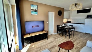 A modern living room with a wooden floor, a TV on a stand, a dining area with a table and chairs, and a kitchen in the background. - Chez Béranger - near train station/congress center (Le Mans)