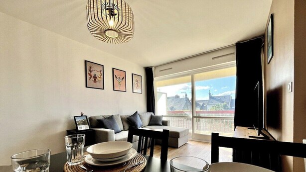 A dining area with a table set for four, a sofa, and a large window with a city view. - Chez Béranger - near train station/congress center (Le Mans)