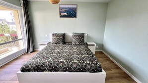 A bedroom with a large bed, a bedside table, a nightstand, a hanging light fixture, and a window with curtains. - Chez Béranger - near train station/congress center (Le Mans)