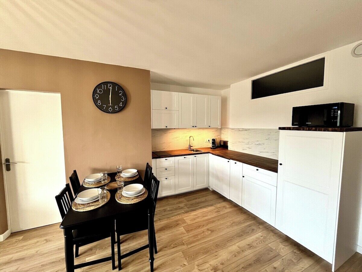 Eine kleine Küche mit weißen Schränken, einer Holz Arbeitsplatte, einer Uhr an der Wand und einer Mikrowelle auf der Arbeitsfläche.