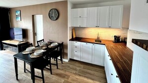 A compact kitchen with white cabinets, a wooden countertop, and a dining area with a table set for four. - Chez Béranger - near train station/congress center (Le Mans)