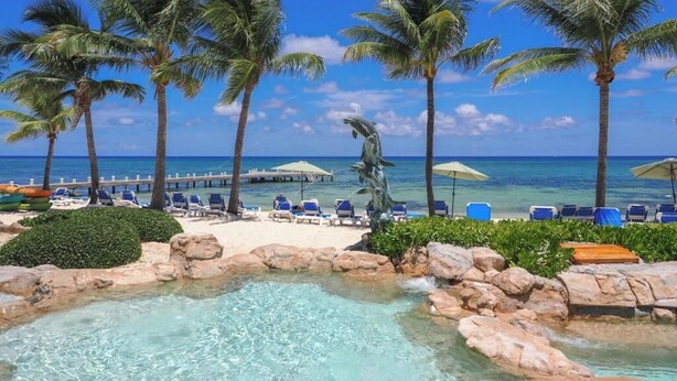 Un resort tropical con piscina cristalina, palmeras y sillas de playa.