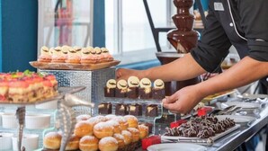 Un bufé con diversos postres, incluyendo pasteles, bollos y brownies.