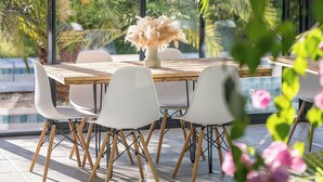A dining area with a wooden table and white chairs, surrounded by glass walls and tropical plants. - NUIKI Lodges (Montsegur-sur-Lauzon)