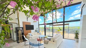 A modern living room with a sofa, chairs, and a TV. There is a balcony with a view of the sky and trees. - NUIKI Lodges (Montsegur-sur-Lauzon)