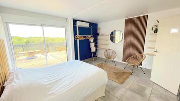 A bedroom with a large bed, a balcony with chairs, a wardrobe, and a mirror.