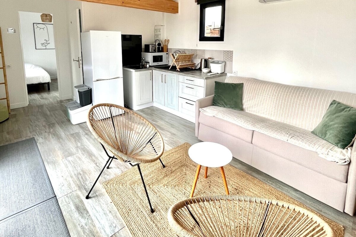 A compact living space with a kitchenette, a sofa, two wicker chairs, and a small round table.