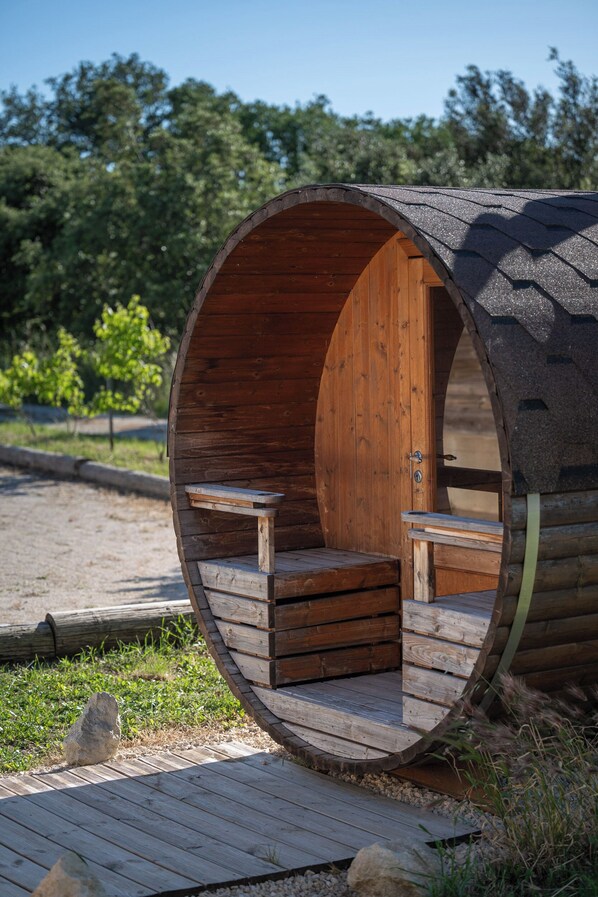 A cylindrical wooden structure with a door and two benches inside. - NUIKI Lodges (Montsegur-sur-Lauzon)
