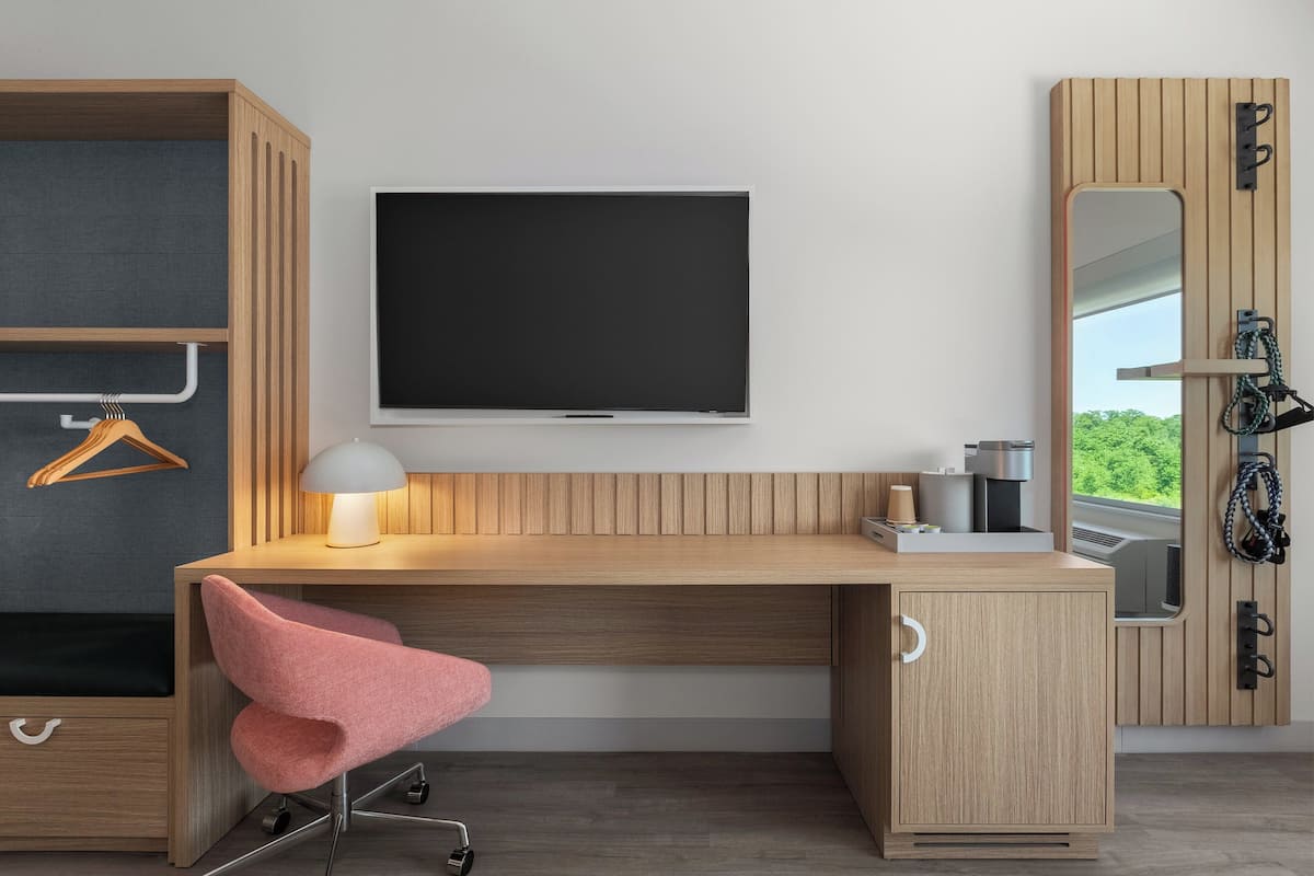 Un dormitorio moderno con un escritorio de madera, una silla rosa, un televisor montado y un armario con espejo.