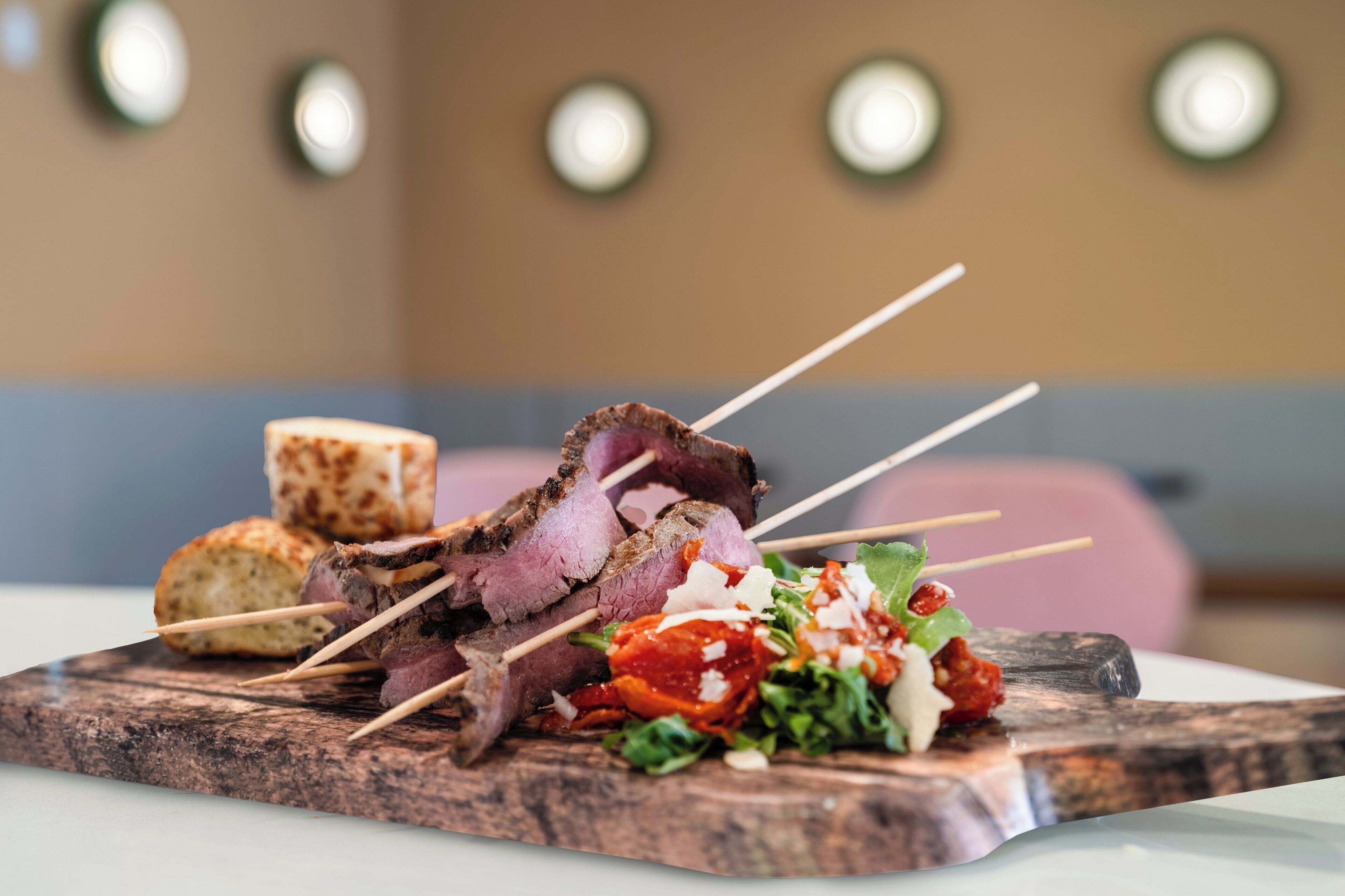 Een houten plank met spiezen vol vlees, een stuk brood en een salade.