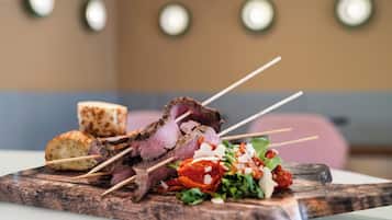 Een houten plank met spiezen vol vlees, een stuk brood en een salade.