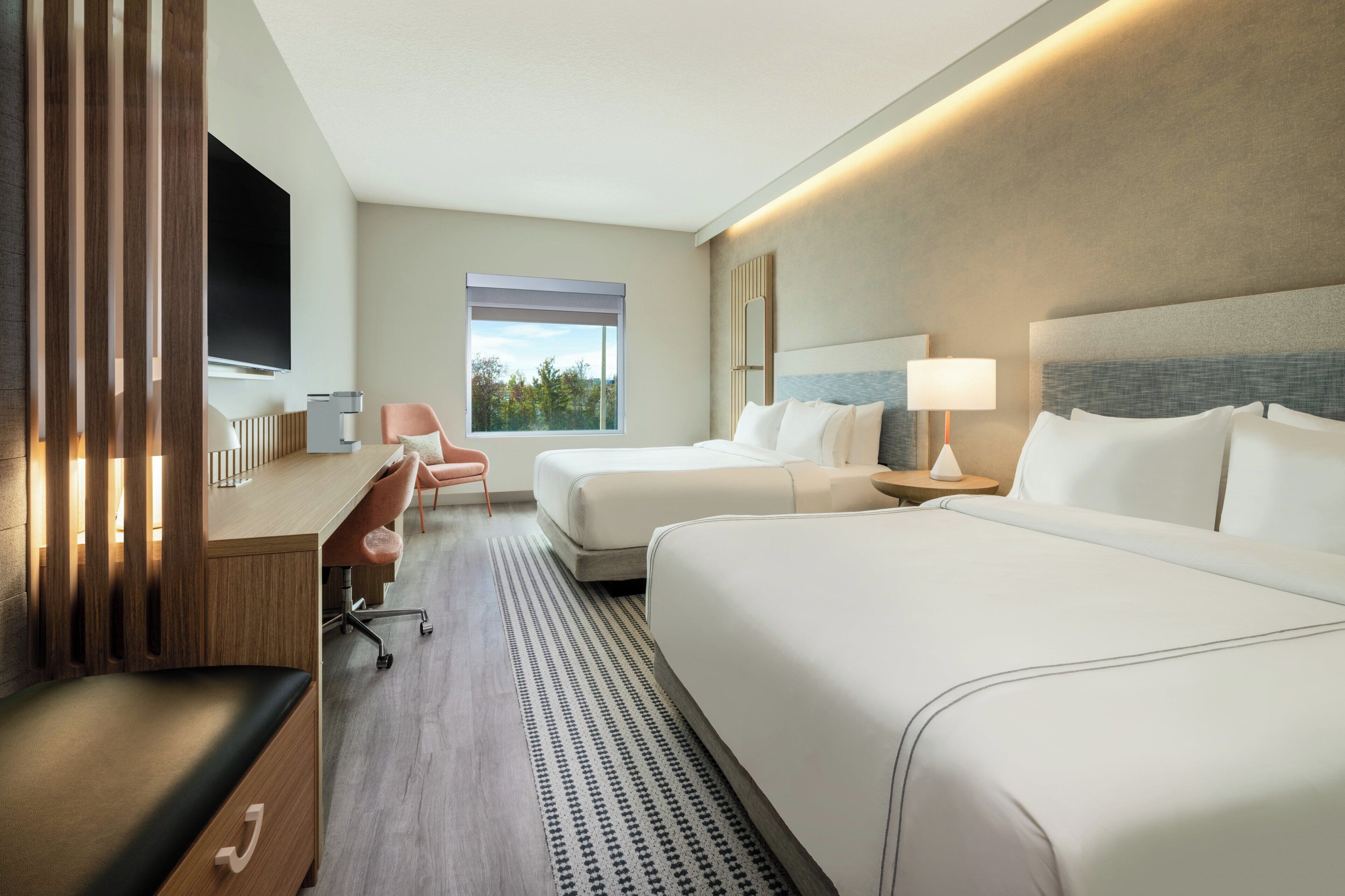 A hotel room with two beds, a desk, a chair, a TV, and a window with a view.