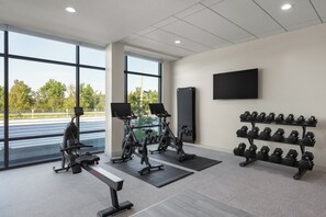 Ein Fitnessstudio mit Cardiogeräten, Hanteln und einem Fernseher an der Wand.