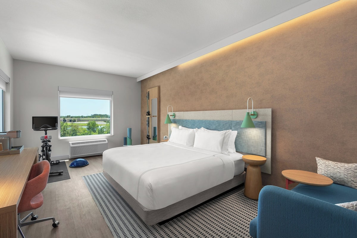 Una habitación de hotel moderna con una cama grande, un escritorio con computadora, un televisor y vistas al exterior.
