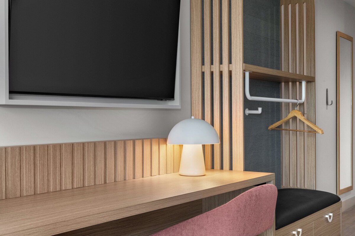 Una habitación moderna con un escritorio de madera, una lámpara colgante, una silla negra y un armario de madera.