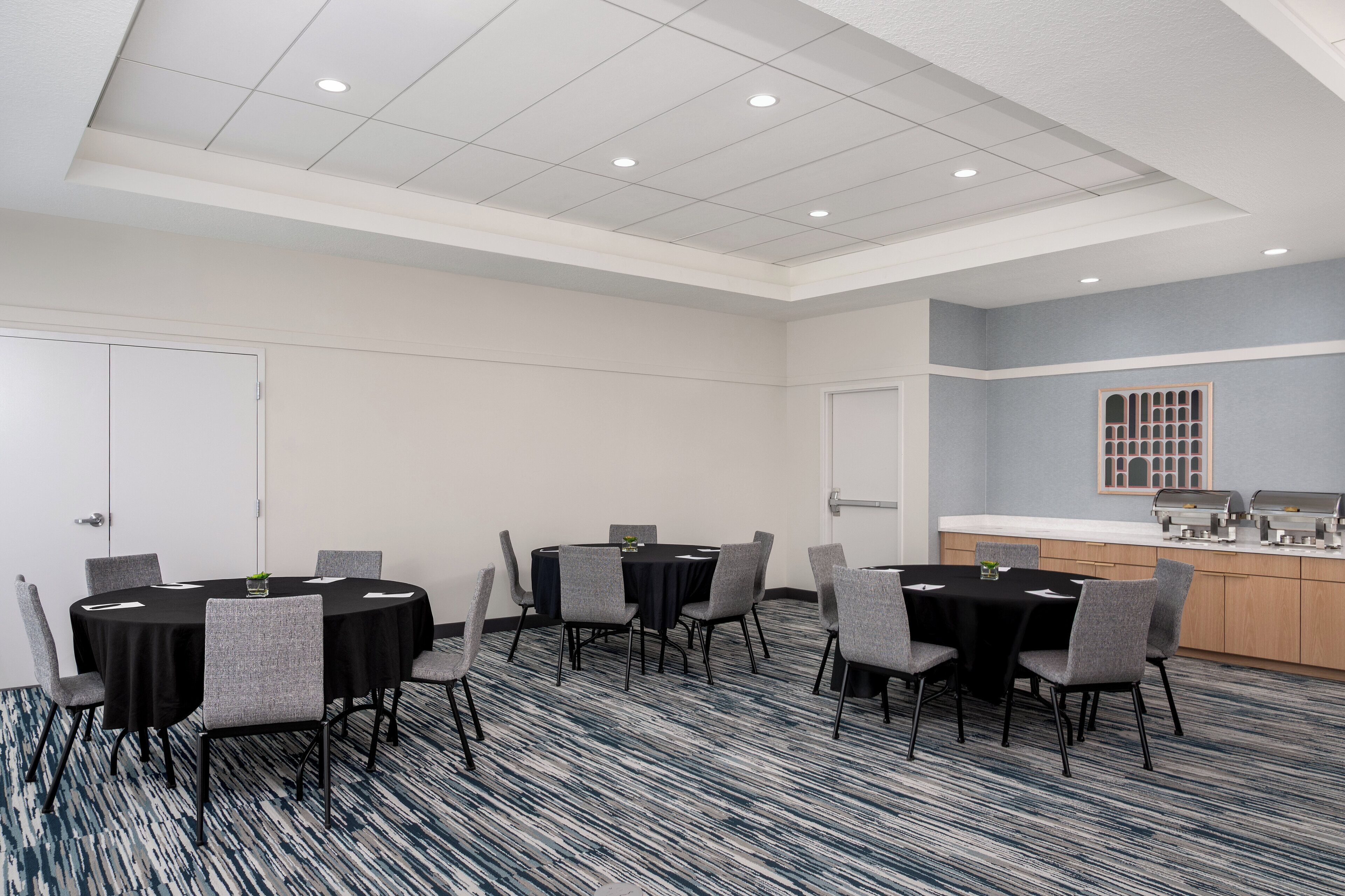 Une salle de conférence équipée d’une table ronde, de chaises, d’un espace buffet et d’un tapis à motifs.