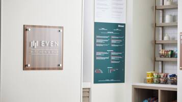 Un letrero que dice 'EVEN KITCHEN & BAR' y un panel con la carta de menú en una habitación con estanterías y almacenaje.