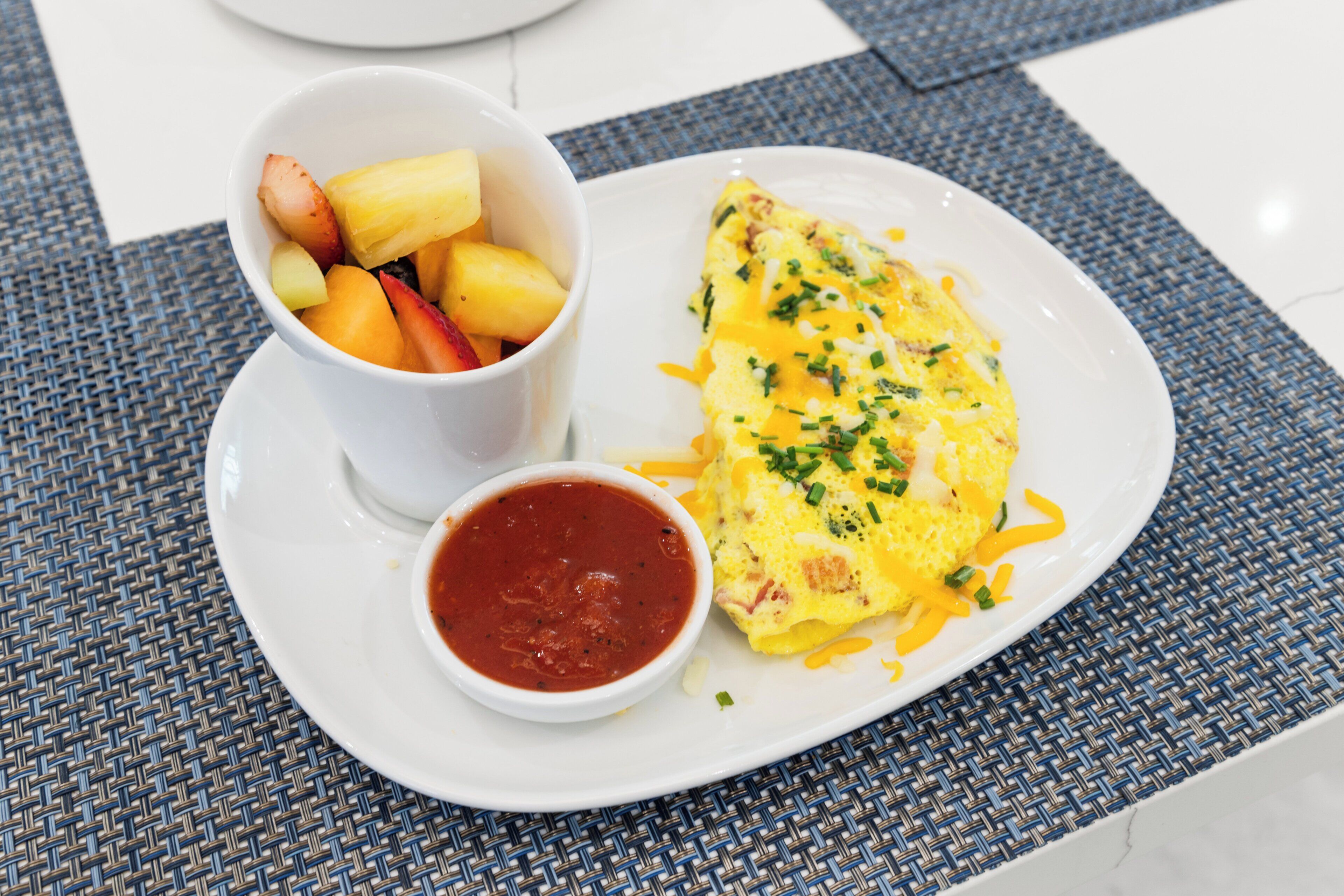 A plate with an omelette, a bowl of fruit, and a small bowl of sauce.