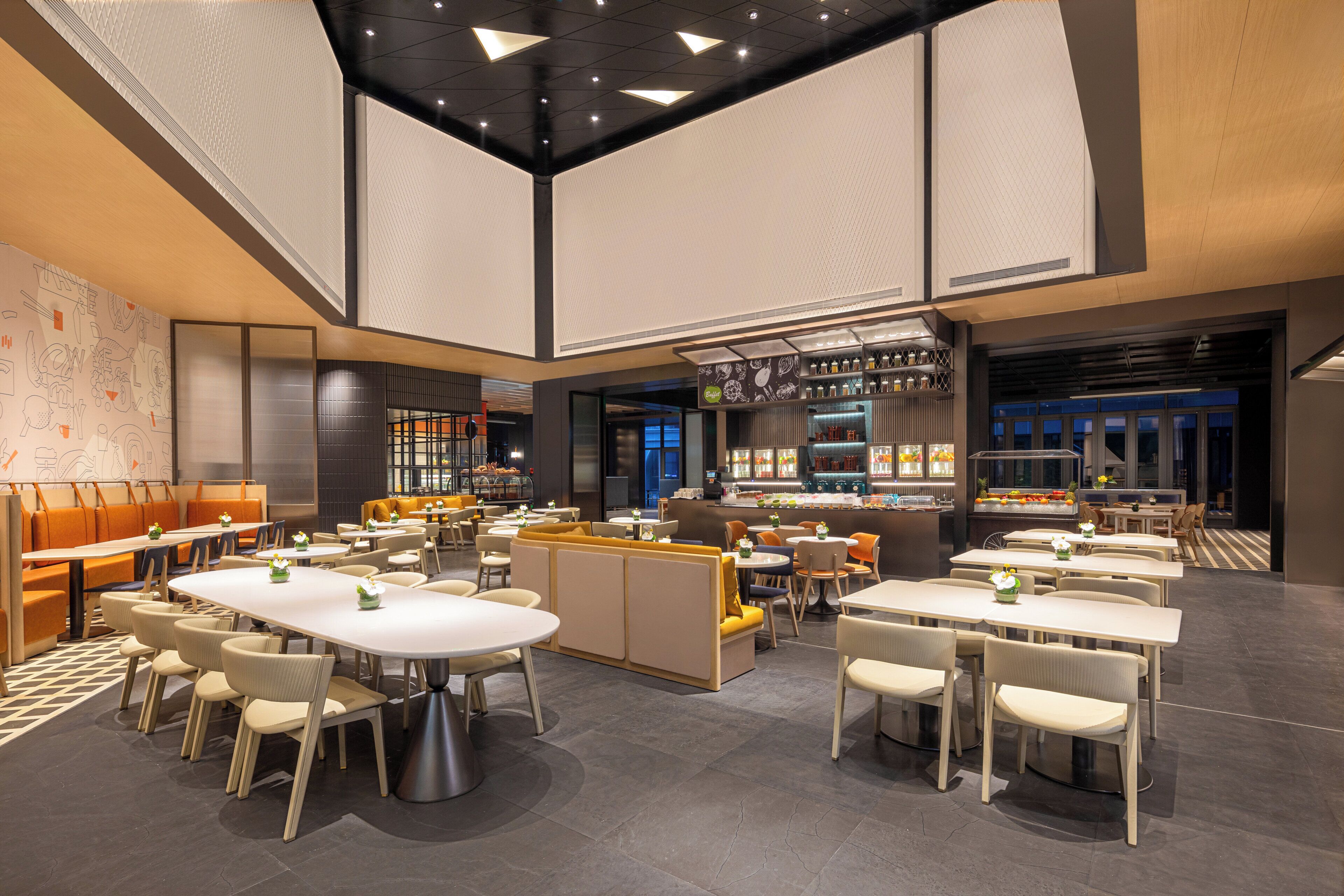 En moderne restaurant med højt til loftet, flere spiseområder og en bar.